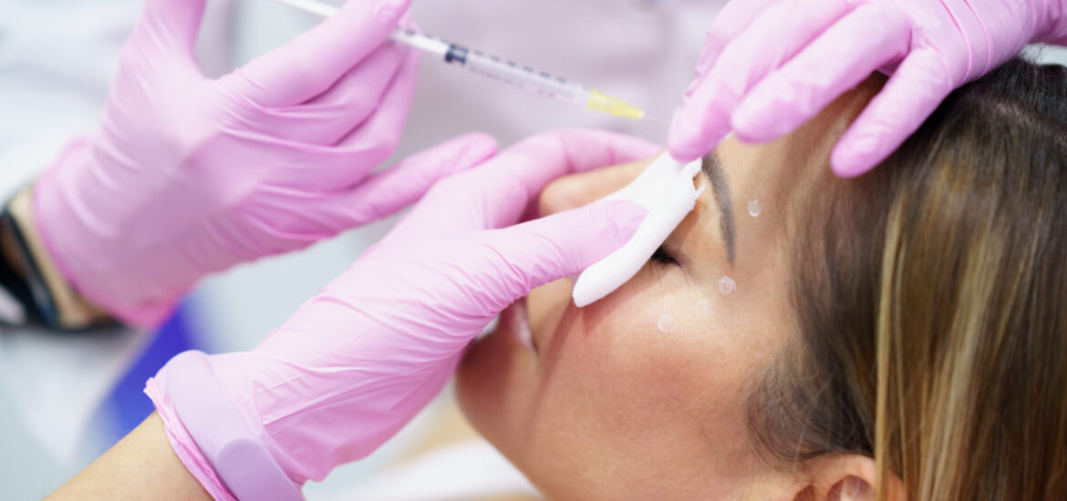 Aesthetic doctor injecting botulinum toxin into the forehead of her middle-aged patient. Facial treatment done in a cosmetic surgery clinic.