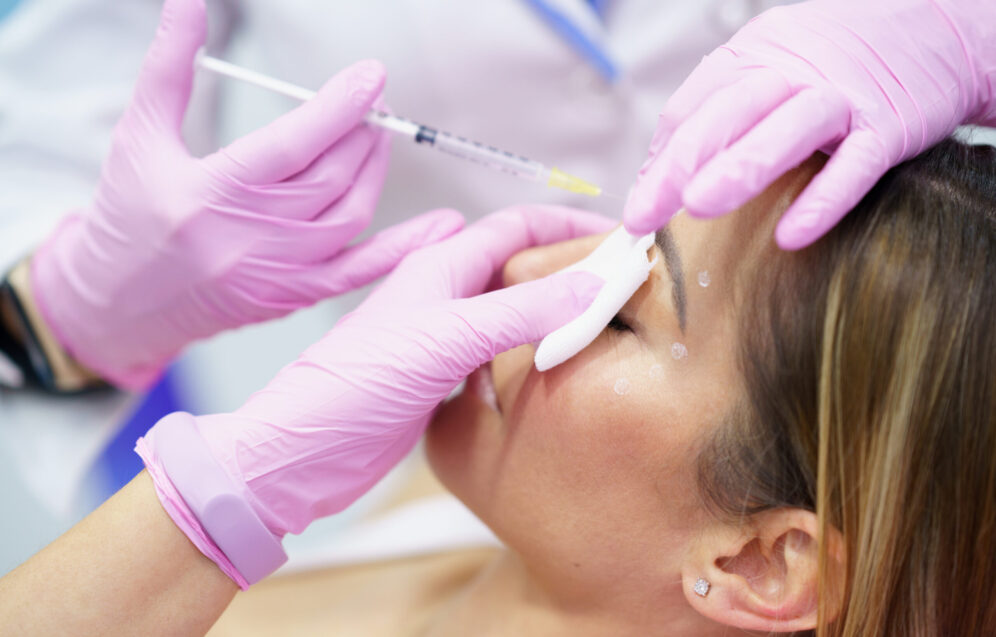 Aesthetic doctor injecting botulinum toxin into the forehead of her middle-aged patient. Facial treatment done in a cosmetic surgery clinic.