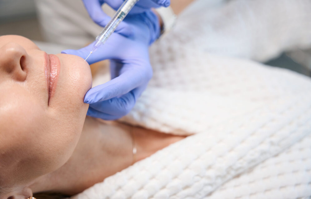 Close up of cosmetologist hands making injection for smoothing wrinkles on mature woman face in beauty salon