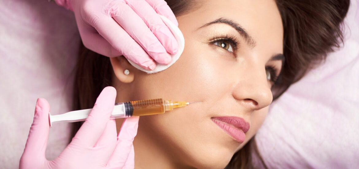 Close-up of beautiful woman getting injection in the cosmetology salon. Doctor in medical gloves with syringe injects cheeks drug.