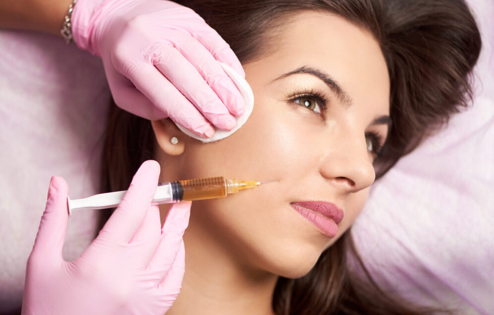 Close-up of beautiful woman getting injection in the cosmetology salon. Doctor in medical gloves with syringe injects cheeks drug.