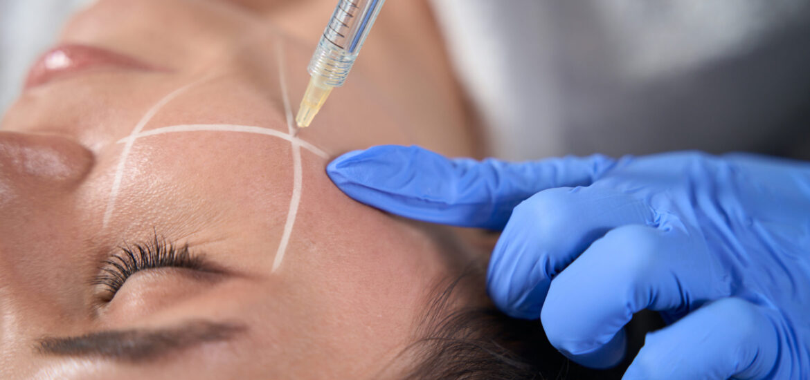 Cosmetologist in protective gloves holding syringe and making beauty injections for face to lady in designated area