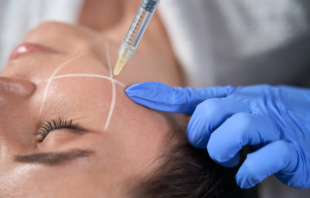 Cosmetologist in protective gloves holding syringe and making beauty injections for face to lady in designated area