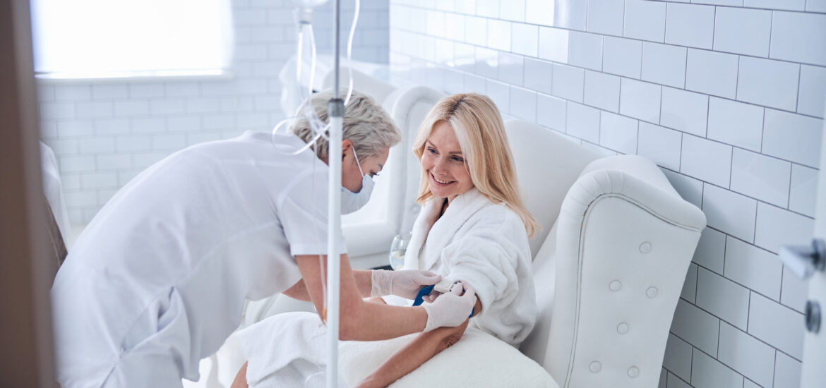 Side view portrait of happy smiling female in white blush bathrobe looking away during the intravenous therapy in medical clinic