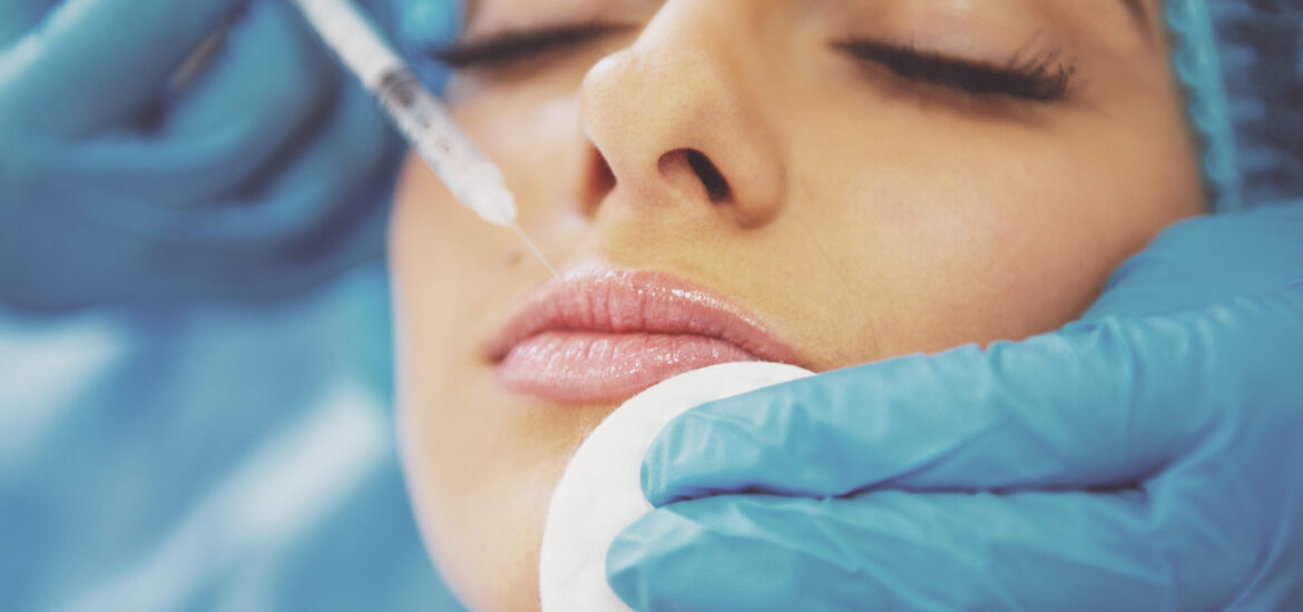 Beautiful young woman is getting an injection in her face, lying with closed eyes, close-up