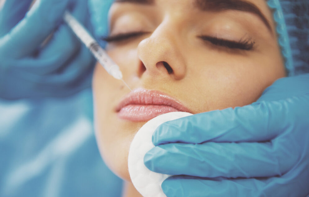 Beautiful young woman is getting an injection in her face, lying with closed eyes, close-up