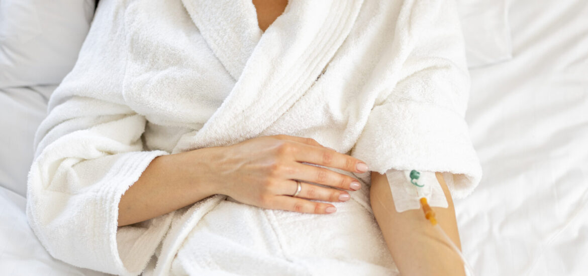 Beautiful woman in white gown with catheter in her arm resting in medical ward. Female patient in comfortable medical suite