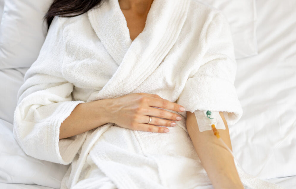 Beautiful woman in white gown with catheter in her arm resting in medical ward. Female patient in comfortable medical suite