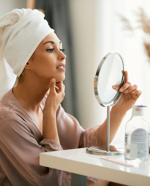 Junge Frau bei der Betrachtung ihres Hautbildes im Spiegel für ästhetische Hautgesundheit bei Juvanity Lampertheim